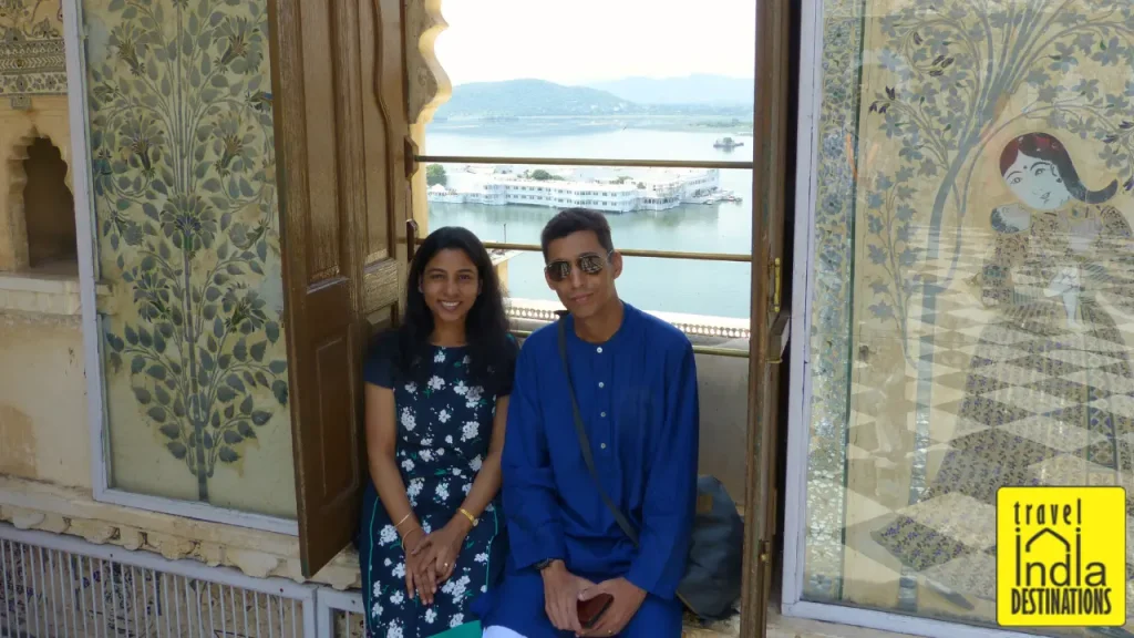 A picture of couple sitting in City Palace with the backdrop of Lake Pichola and Lake Palace, one of the best places to visit in Udaipur.