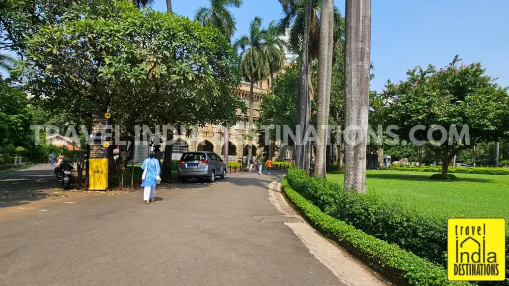Visitors walking along the garden pathway from the booking office toward the main entrance of CSMVS on a sunny afternoon.