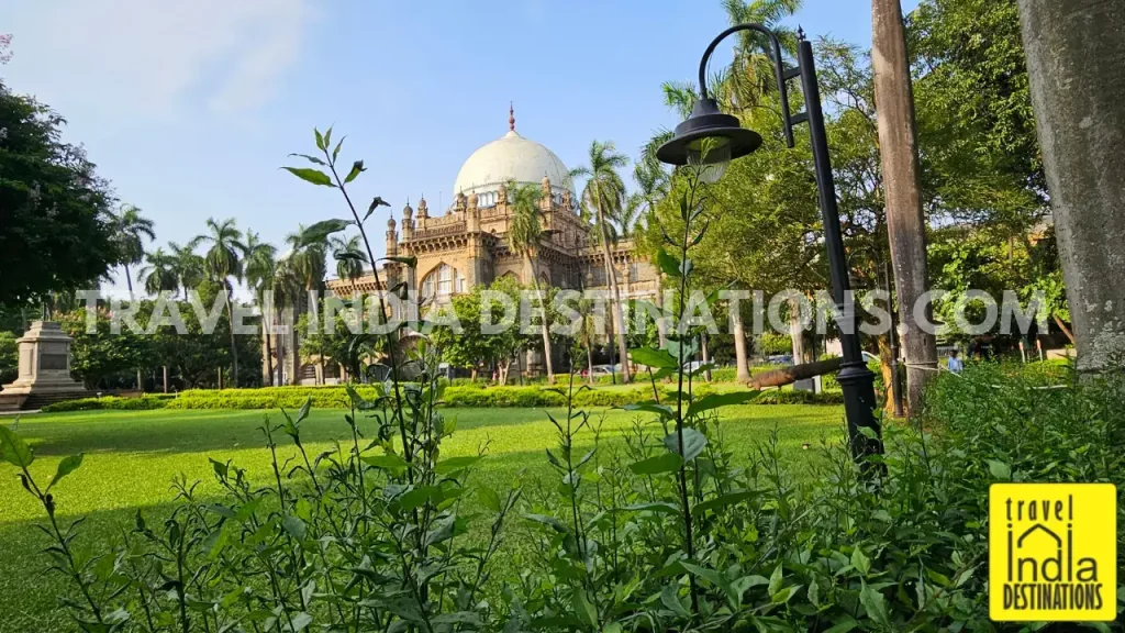 Chhatrapati Shivaji Maharaj Vastu Sangrahalaya seen from the garden, with its white dome gleaming in the evening sunlight, framed by plants and a garden lamp post.