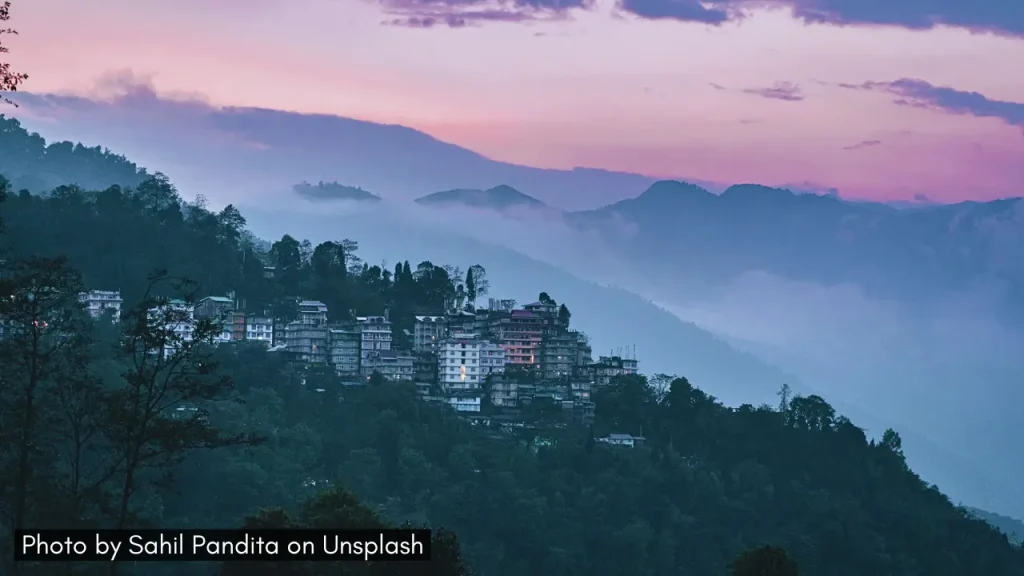 A shot of Gangtok Sikkim with misty mountains and lush greenery and pink sunset sky ideal for honeymoon in April in India.