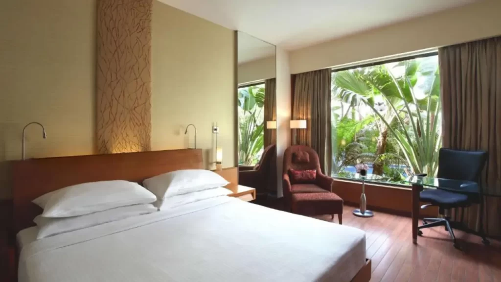 Room at Hyatt Pune with white bedding, armchairs, and palm tree view