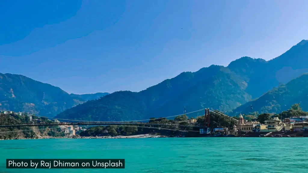 A panoramic shot of Rishikesh with the Lakshman Jhula bridge, river Ganges and the surrounding lush hills, one of the best minimoon destinations in March in India.