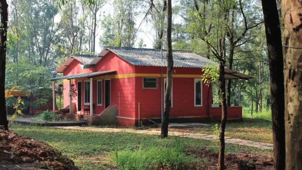 Red jungle cabin surrounded by tall trees at The Jungle Resort Amba Ghat one of the hotels near ghats in Maharashtra